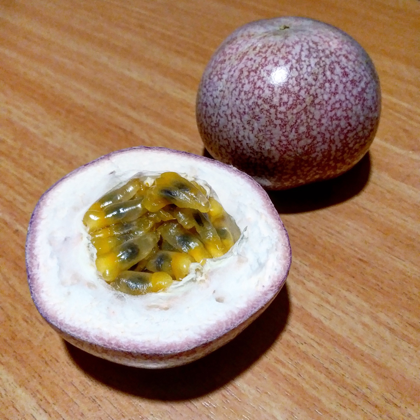 Whole and halved purple passion fruit showing yellow pulp and seeds