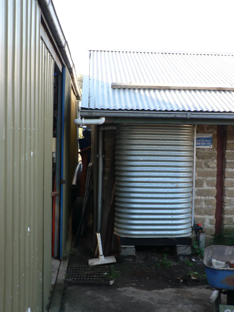 A corrugated steel rainwater tank fed by a downspout beside a house